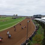 dirt track with horses people tractor van on with people watching behind fence