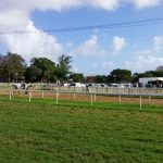 dirt horse track with white fence and tents on one side